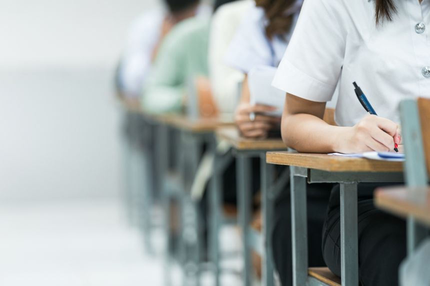 Students Taking Exam in Classroom Setting. Students in uniforms are seated in a classroom, writing answers during an exam, highlighting focus and academic testing.
