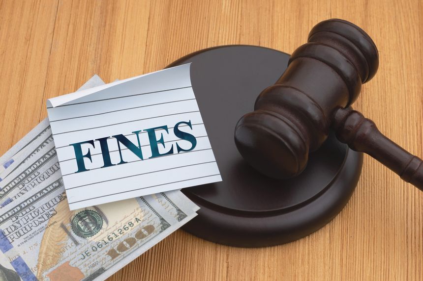 Fines message with judge gavel and block with money on wood desk for penalties, legal fees, court charges, and financial consequences