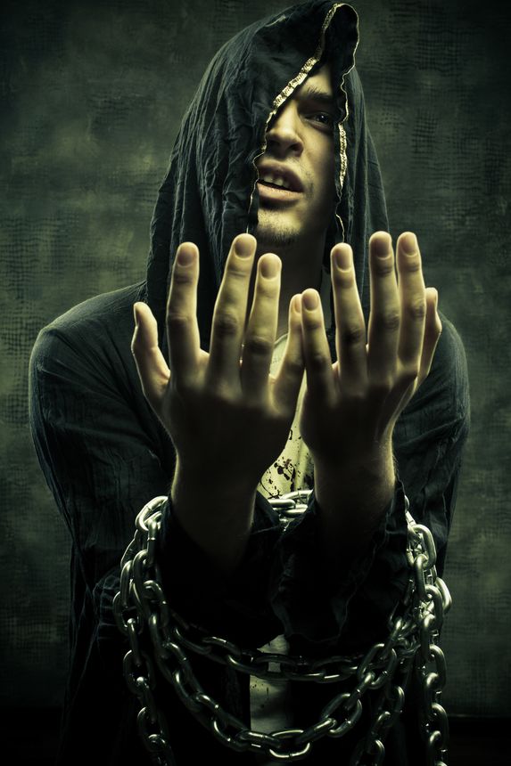 Portrait of miserable fanatical young man in hood bounded by chains.