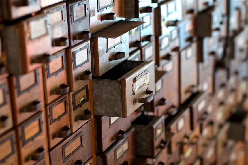 A shot of a card catalog with an open drawer central to the image.  There is a pleasing bokeh as the details fade to the background, focusing attention to the main subject.  Taken with a DSLR using a Nikkor 50mm f/1.4D lens.