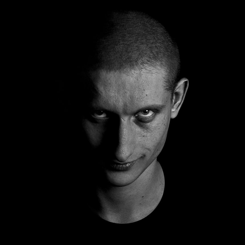 Grimly grinning man looks into the camera. Studio portrait in low-key on black background