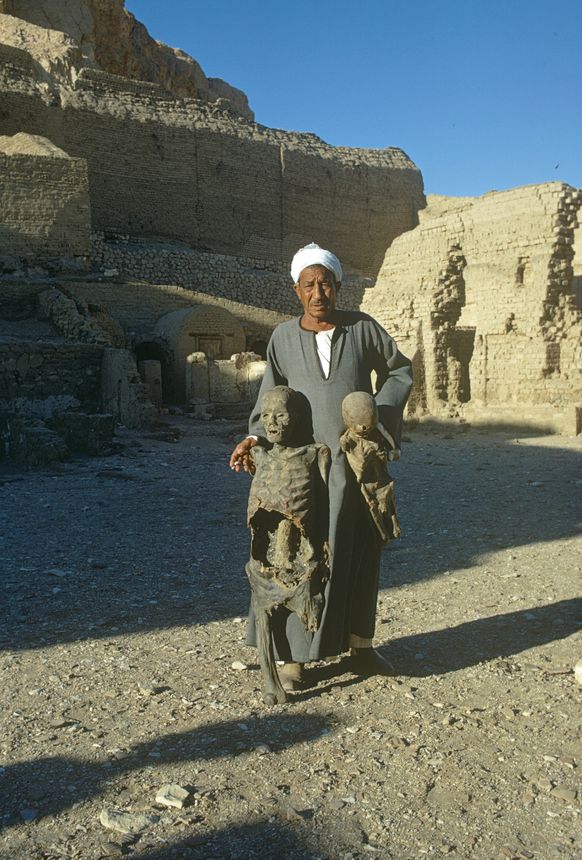 Egypt, 1972. Egyptian guide presents tourists at an ancient site dried human remains.